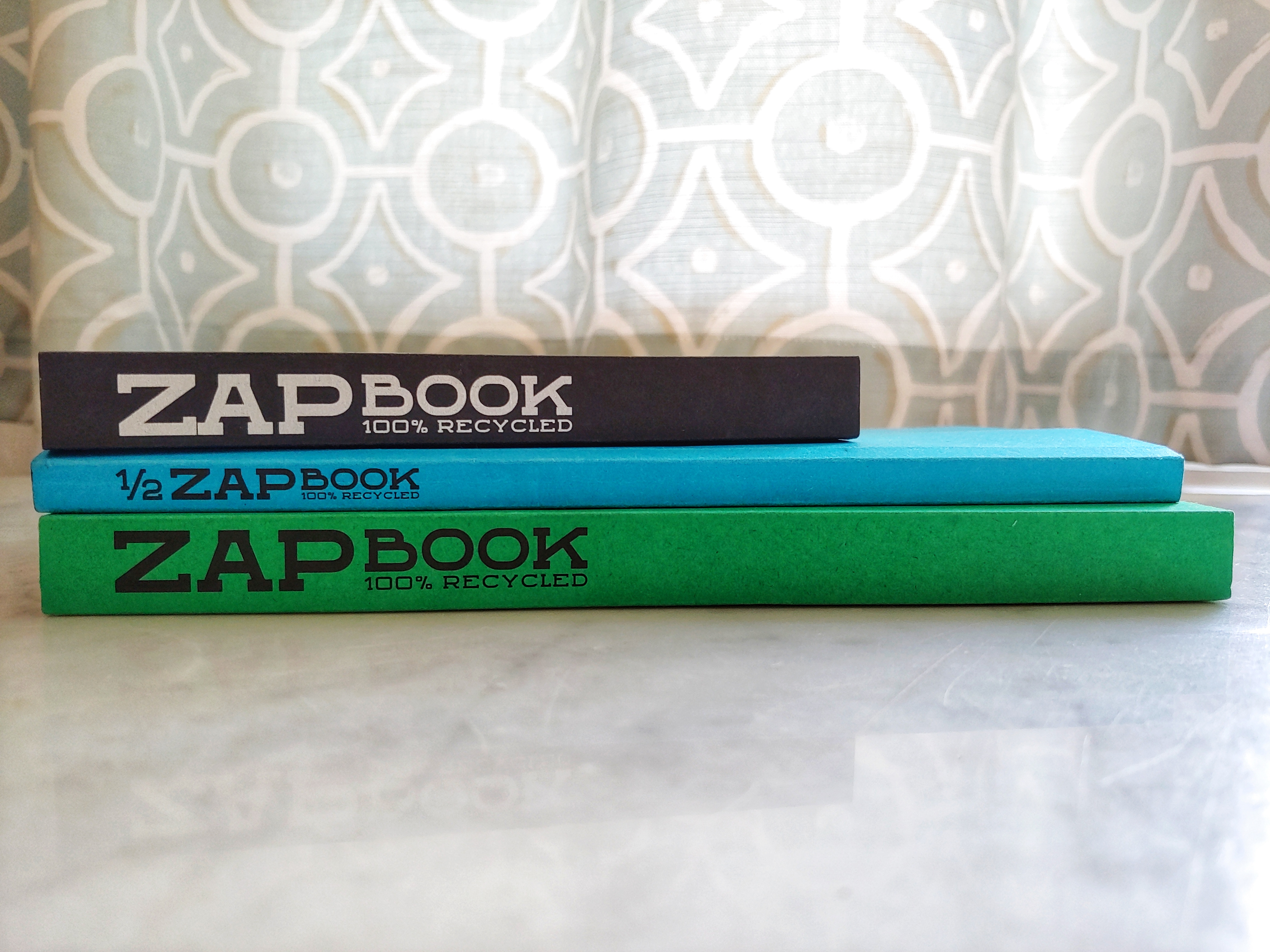 Three Zap Books on their side showing their spines which read 'Zap Book 100% Recycled'