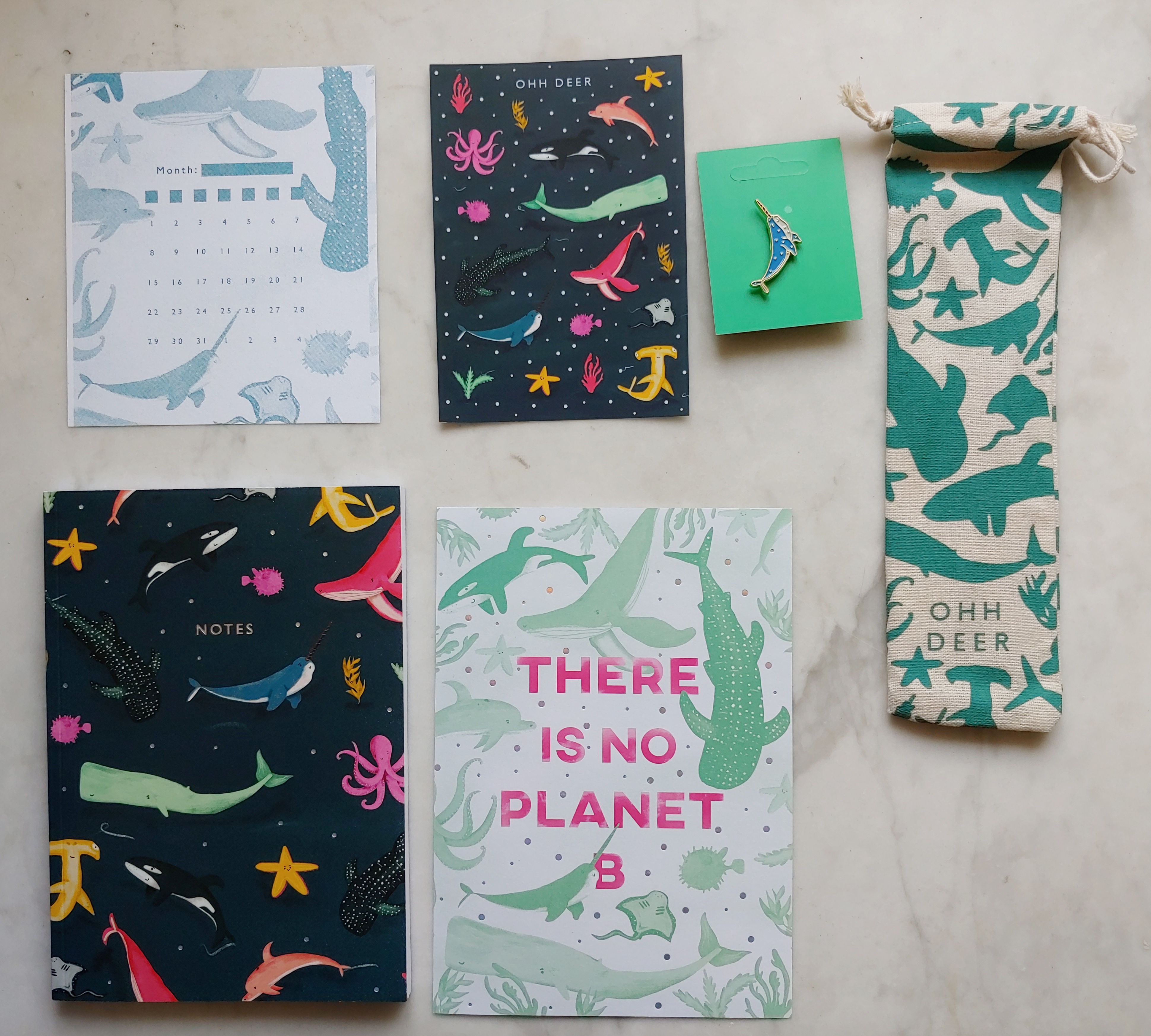 Small single-month calendar sheet, page of stickers, notebook, poster reading 'there is no Planet B', narwhal pin, and bag containing metal straws, all in various whale-based patterns
