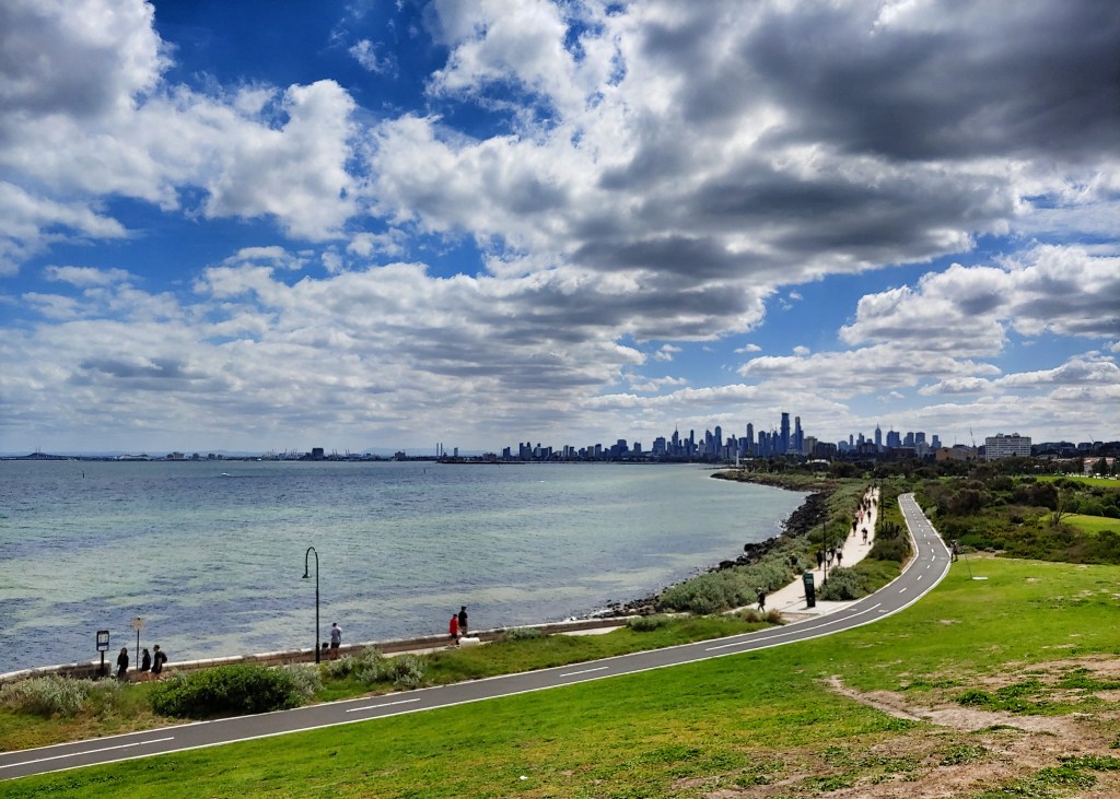A view of the sky and Melbourne Central Business District from Elwood Beach.  A bright blue sky is seen above a silhouetted skyline.