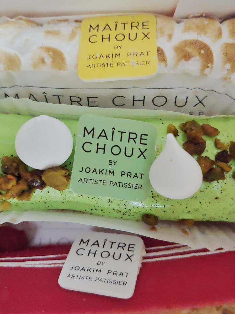 Close-up photo of three eclairs, one with a meringue topping, one with a green icing topping, and one with a matte pink topping.