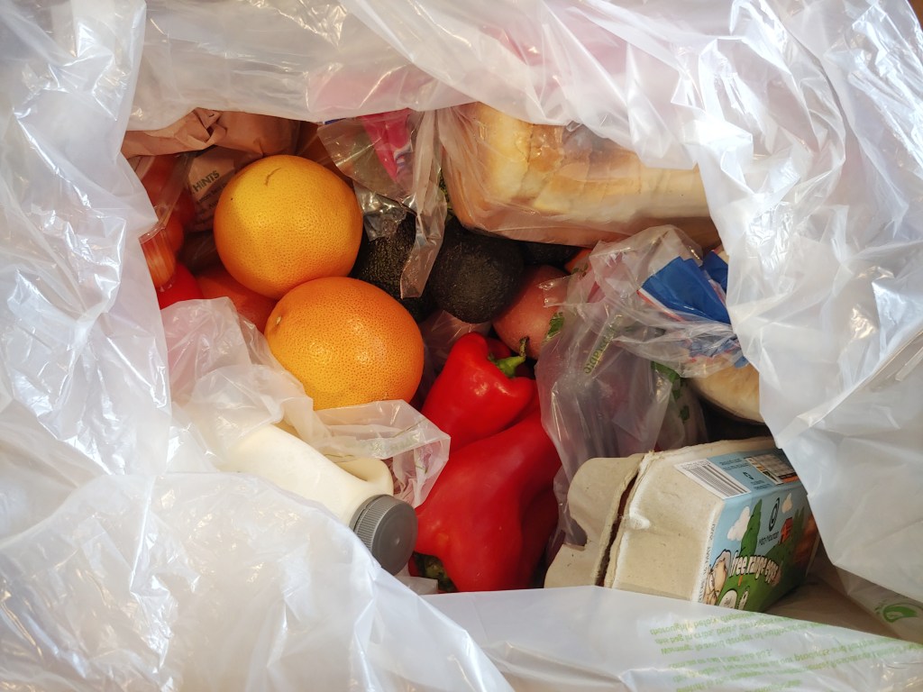 Looking into the opened Jim's Home Fresh delivery box, with milk, eggs, red bell peppers and grapefruit among others.