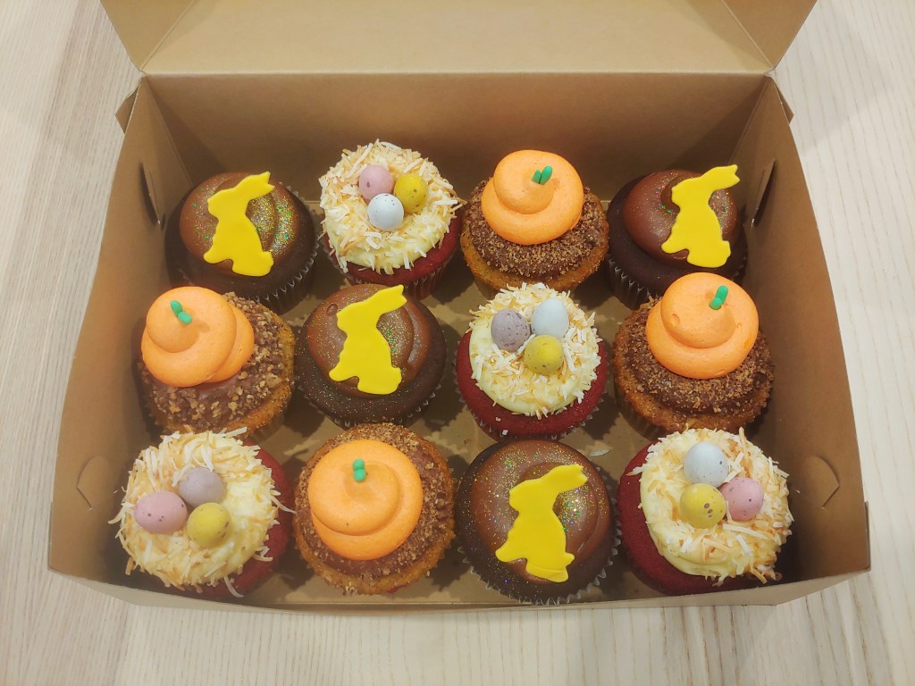 Top down view of a box of 12 Easter themed cupcakes.