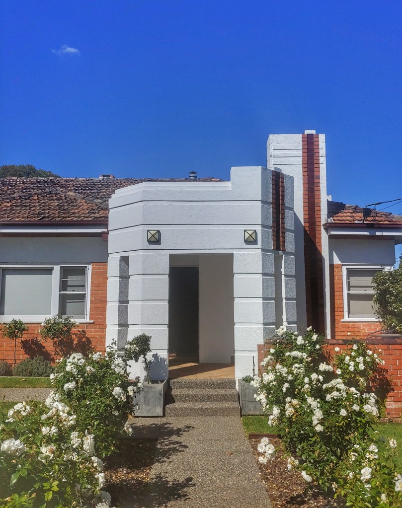 Red brick bungalow with white art deco style porch.