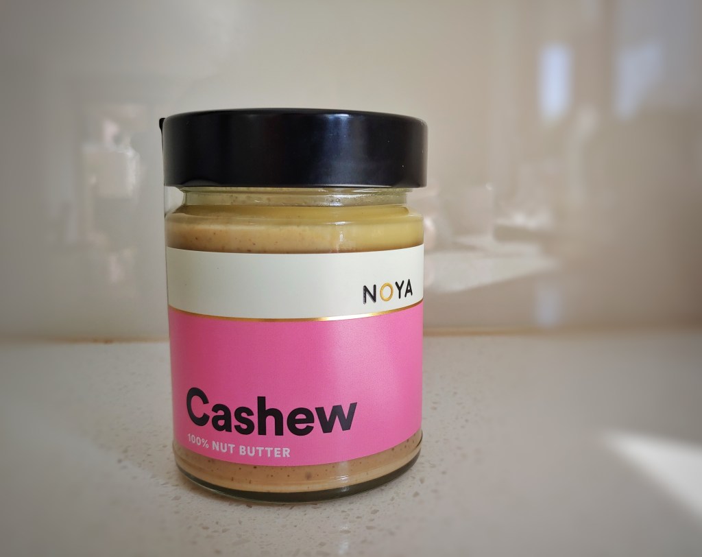Jar of Noya cashew butter with a bright pink label and a black lid.
