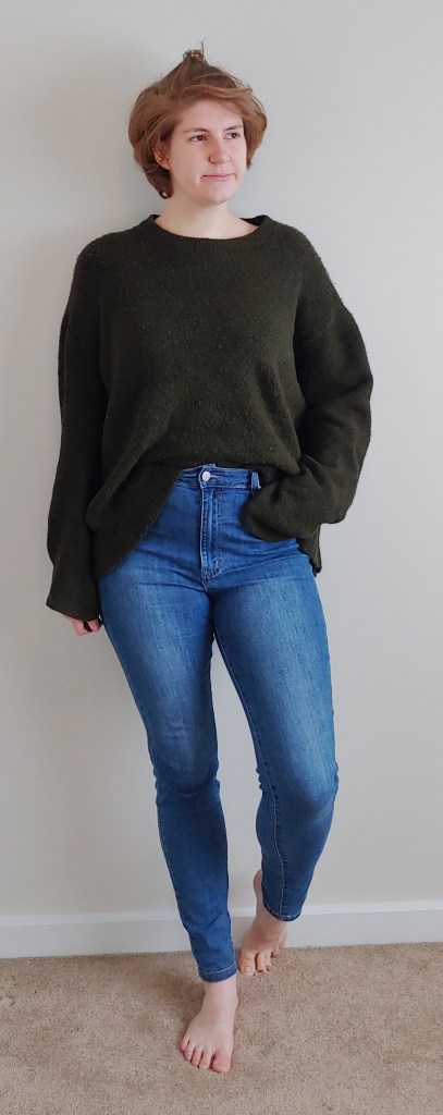 Full length photo of Helen wearing a chunky oversized khaki green jumper, with blue skinny jeans.