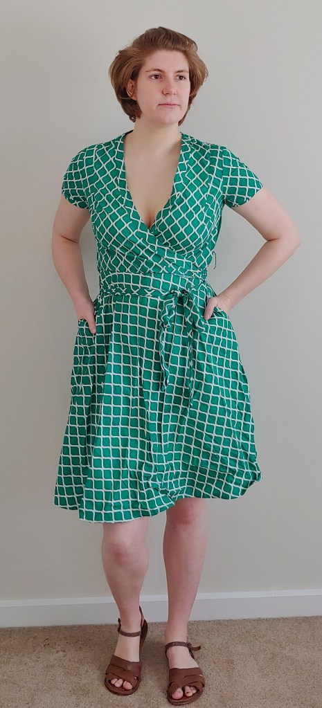 Full length photo of Helen wearing a green a-line wrap dress with a white trellis pattern.