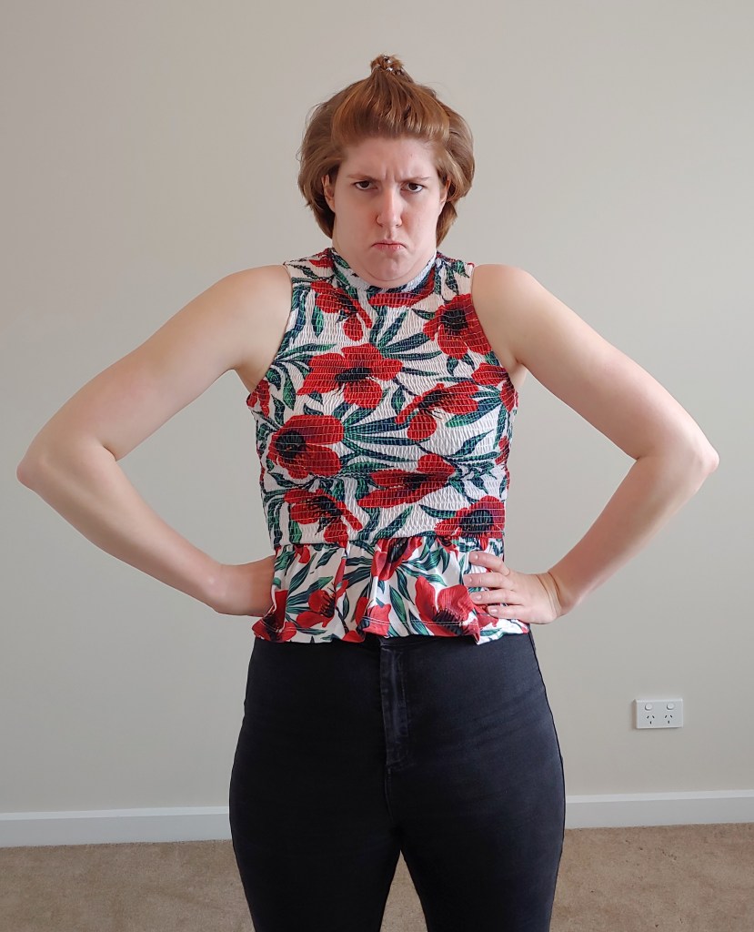 Closer up photo of Helen wearing the same top, with hunched shoulder and arms out to emphasise her neck region.