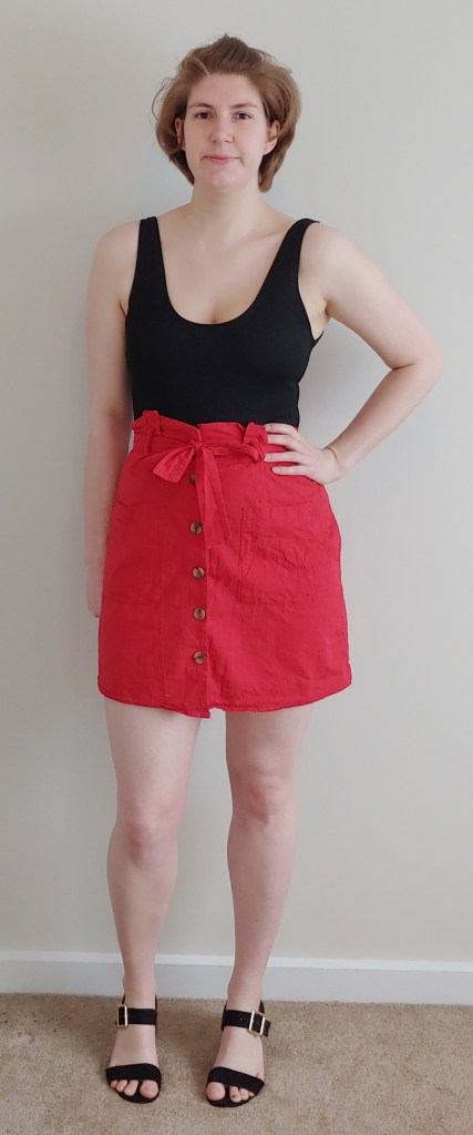 Full length photo of Helen wearing a bright red A-line skirt mini-skirt with a black vest top.