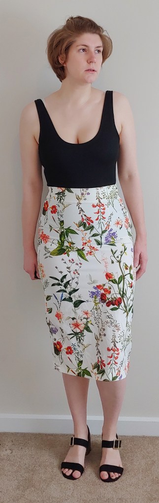 Full length photo of Helen wearing a high waisted botanical print skirt with a black vest top.