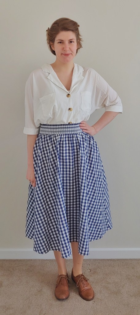Full length photo of Helen wearing a cream half-sleeved shirt with a blue and white gingham knee length circle skirt.