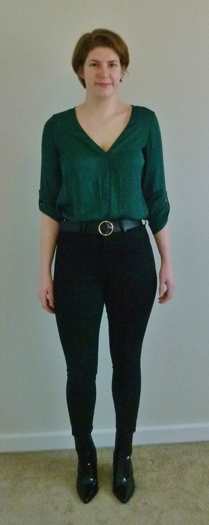 Full length photo of Helen wearing a green silky, three-quarter length sleeved V-neck top, black high-waisted skinny jeans, and black croc-effect boots.