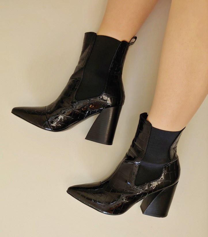 Close up of Helen wearing shiny black crocodile-skin look pull on boots with a chunky heel and pointed toe.