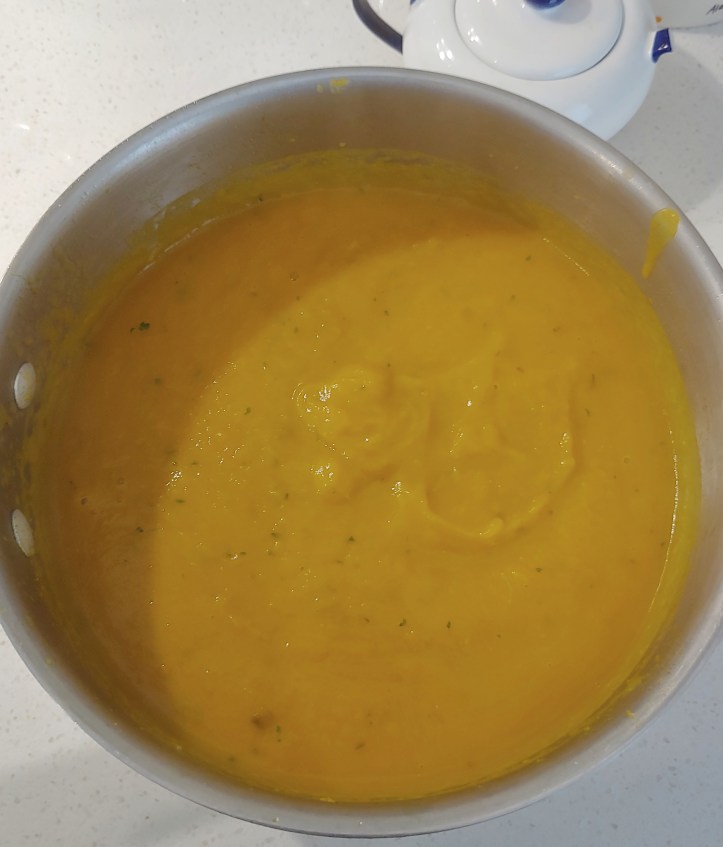 Smooth orange coloured soup in the stainless steel pan.