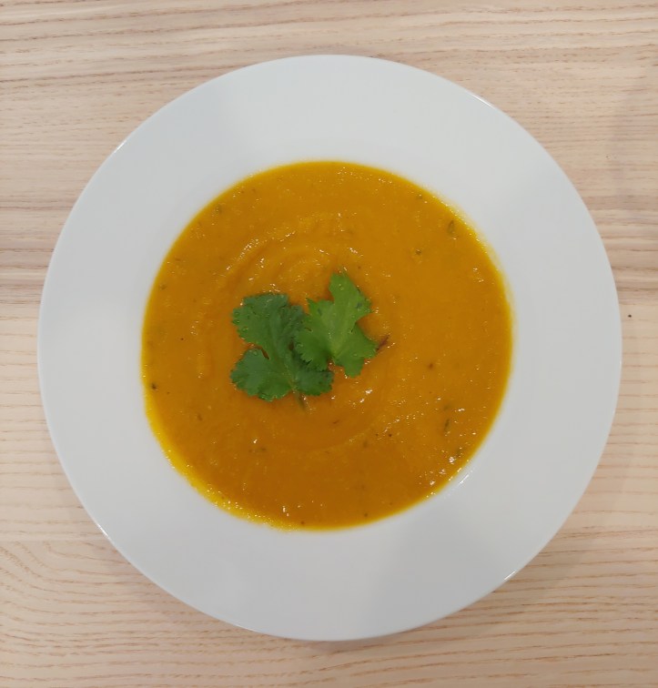 White soup bowl full of a thick orange-coloured soup garnished with two large coriander leaves.