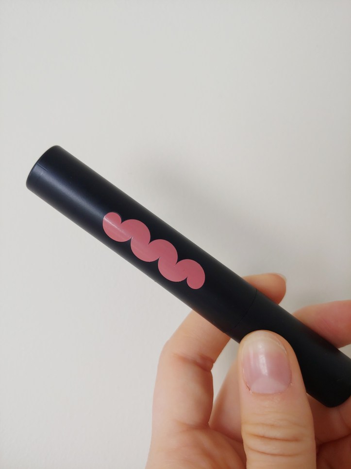 Close up of the black tube of lipstick with a pink squiggle of label to indicate the colour.