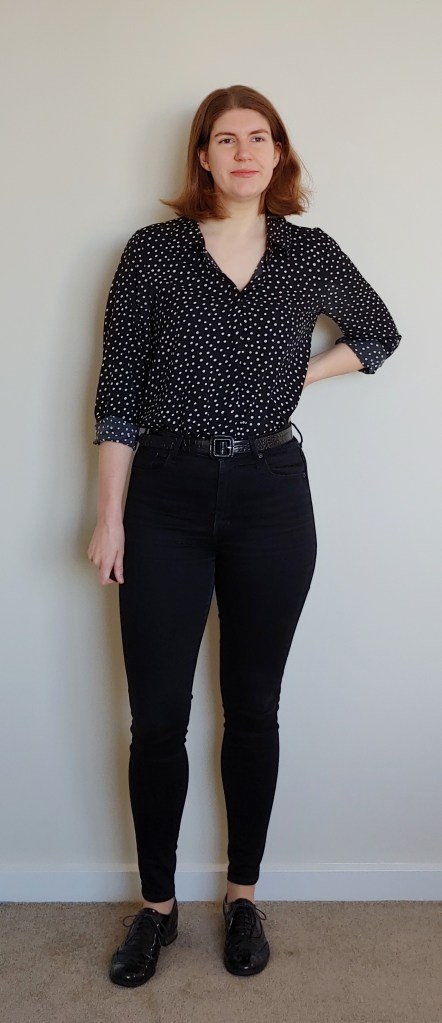 Image of Helen wearing black skinny jeans and a black button-down shirt with white polka dots and the sleeves rolled halfway up her arms. She also wears black patent brogues and a black belt.