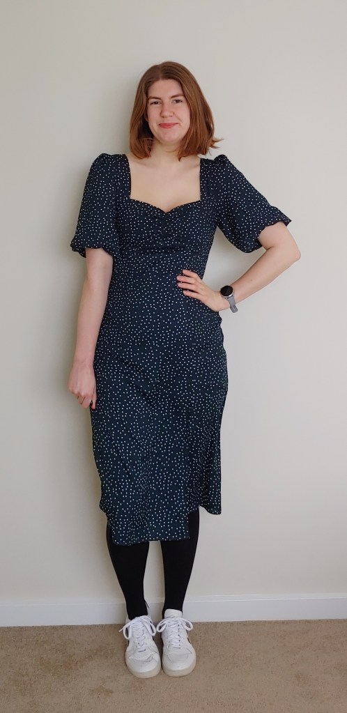 Image of Helen wearing a dark green mid-length dress with small white polka dots, with black rights and white sneakers.