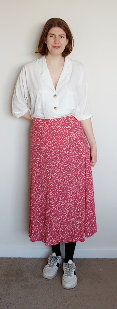 Helen wearing a white shirt with deep lapels and a red and white printed midi skirt, with black tights and white sneakers.