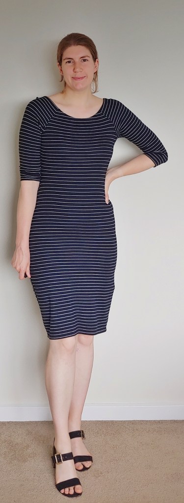Full-length photo of Helen wearing a black dress with thin white horizontal stripes, a boat neck, and elbow length sleeves. She also wears black block-heeled sandals.
