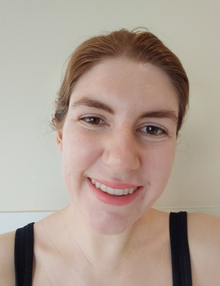 Frontal portrait photo of Helen, with her hair tied back, with slightly peachy-pink lips and full brows, in an open-mouthed smile.