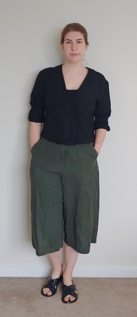 Helen wearing a half-sleeve V-beck top with black tank-top underneath, and calf-length wide-leg khaki culottes, with black flat crossover sandals.