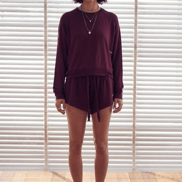 Frontal photo of a model wearing a loose fitting, long-sleeved sweatshirt in a burgundy/maroon colour.