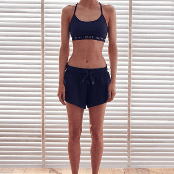 Frontal image of a model wearing a dark blue bralet with thin straps and a wide elastic support with 'MAEVA' written on it.