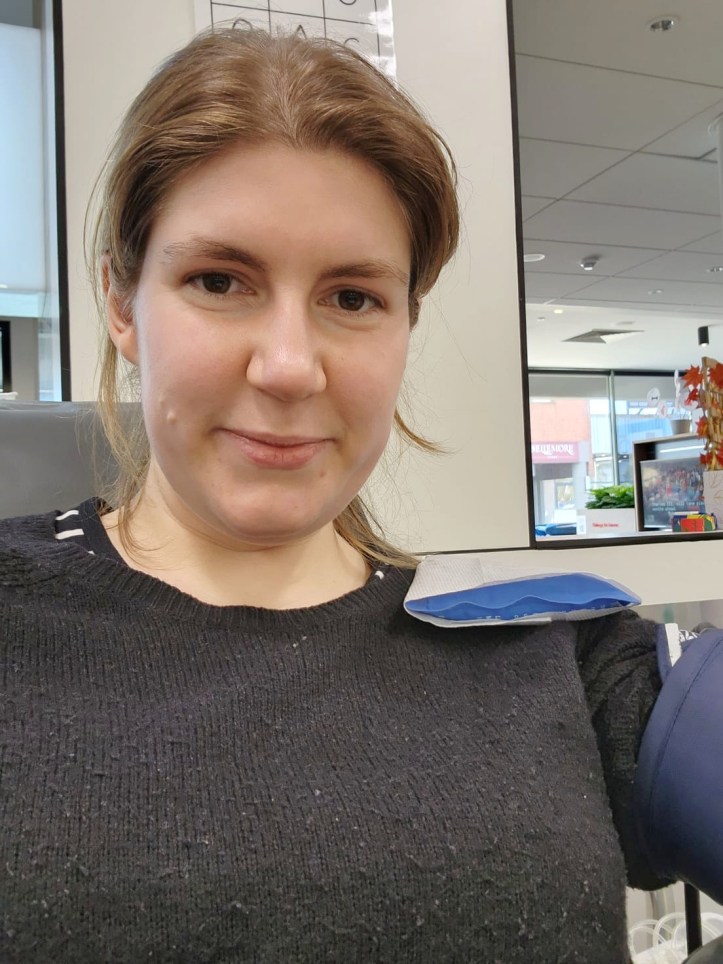 Headshot of Helen in the seat giving blood, with blood pressure band visible on arm, but no needles or blood on show.