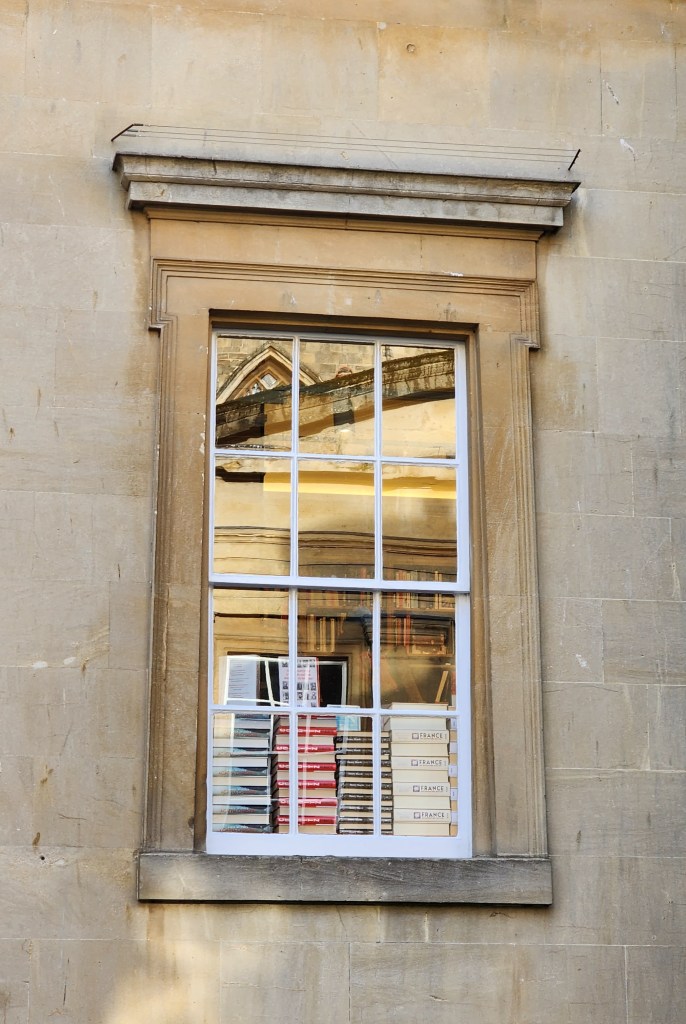 External view of a sash window in a classical style, with piles of books visible on the inside.