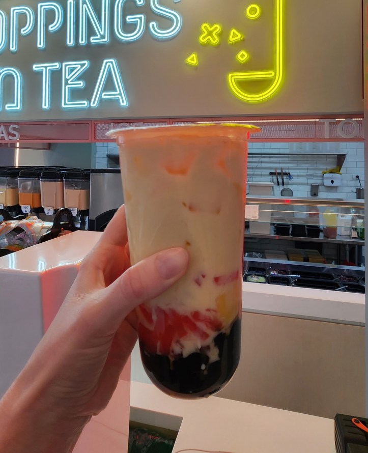 Helen holding up a large cup of bubble tea with various fillings and toppings in colourful layers.