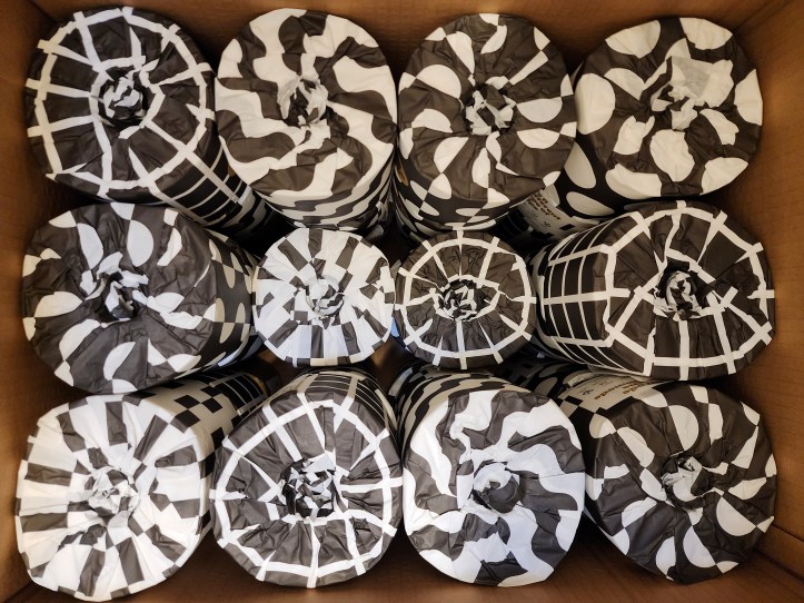 Top-down view of a box full of toilet paper wrapped in black and white patterned packaging.