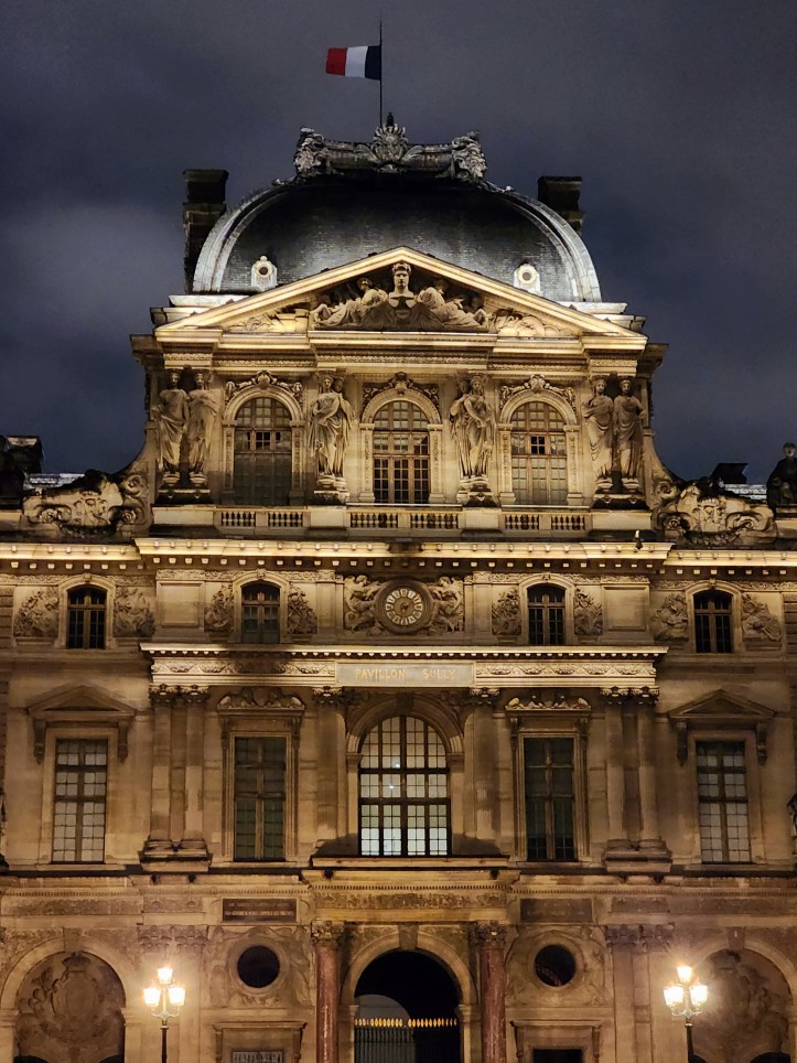 A multi-storey ornate building with Greek columns, a clock, and a rectangular domed roof.