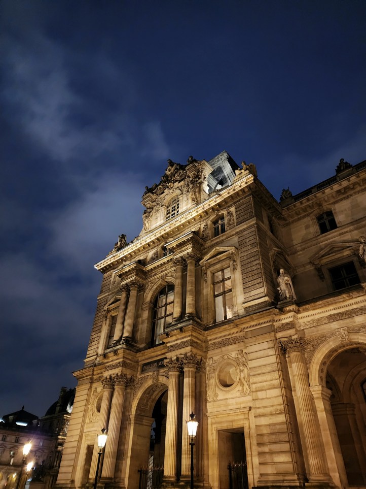 A view up to a large, Greco-Roman style  building, with ornately carved window surrounds.