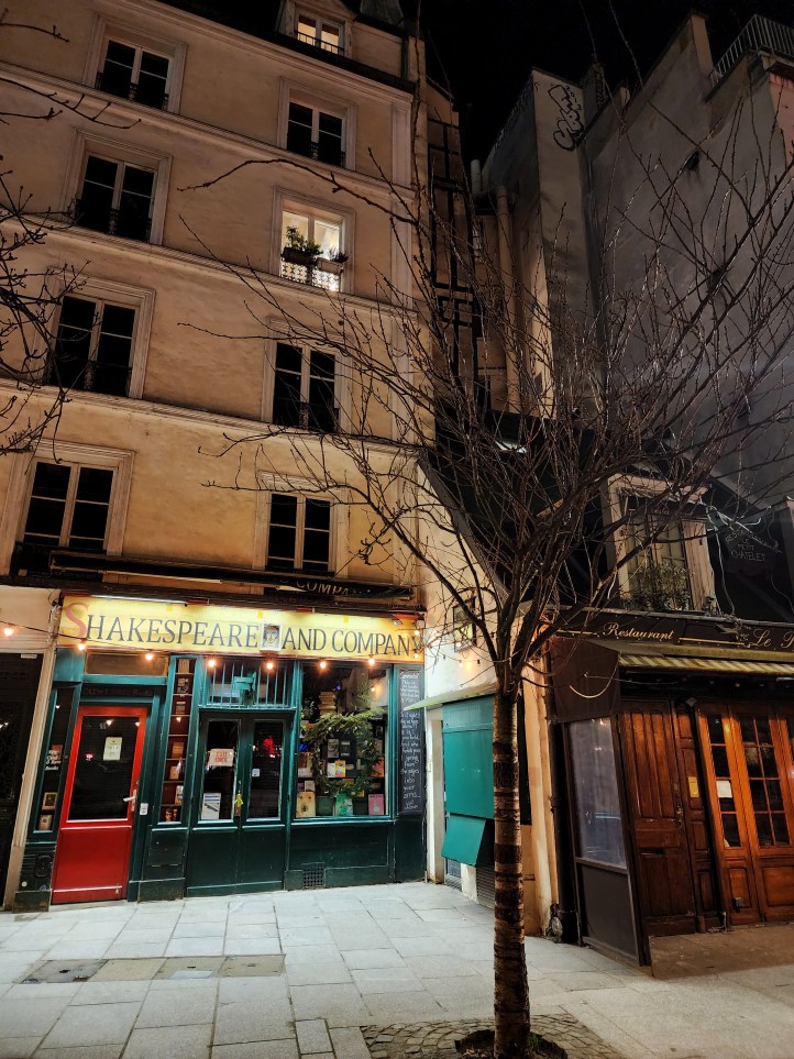 View of the Shakespeare and Company bookshop building, with a small, leafless tree in front, and the five storeys of windows above the shop front.