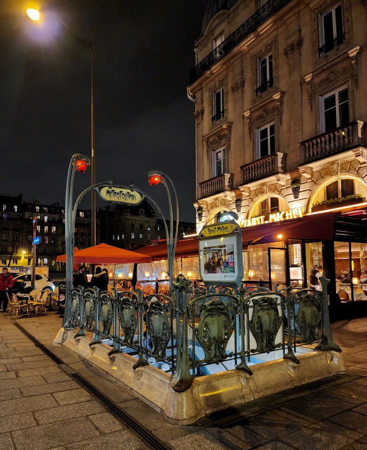 AN art nouveau metro station entrance, with a townhouse building behind on the right.