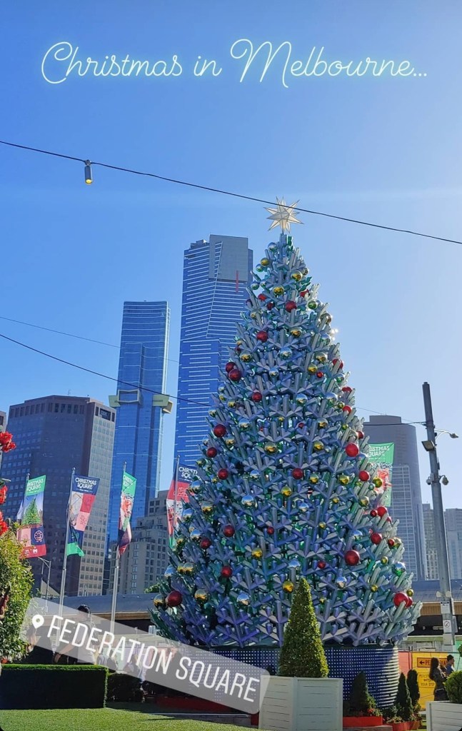 The Christmas decorations at Melbourne's Federation Square, with a large silver and green plastic light up tree covered in red, silver and gold baubles on the right, and skyscrapers on the left.