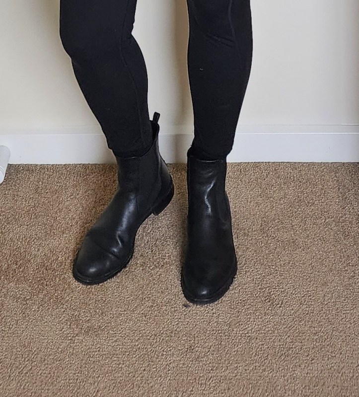 Close-up cropped image of a pair of Helen wearing a pair of black ankle length flat Chelsea boots.