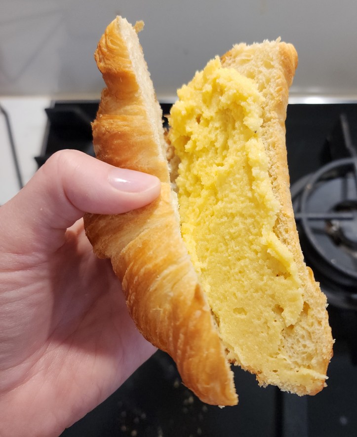 Helen's hand holding a crescent-shape croissant that has been cut open and spread with butter-yellow frangipane.