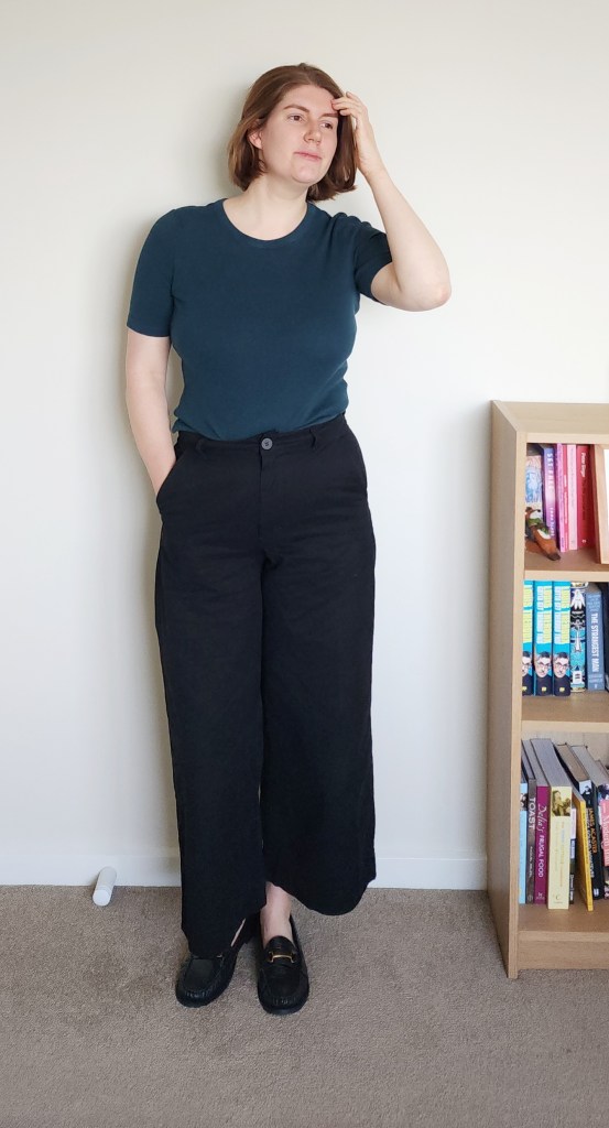 Helen wearing black wide trousers with a green/blue tight t-shirt, and black loafers.
