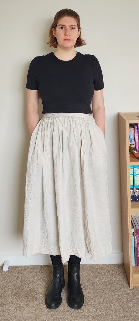 Helen wearing a creamy mid-calf length linen skirt with a tight black t-shirt, black tights, and black chelsea boots.