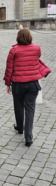 A full-length photo of Helen from behind wearing black jeans and boots, and a burgundy red down jacket.
