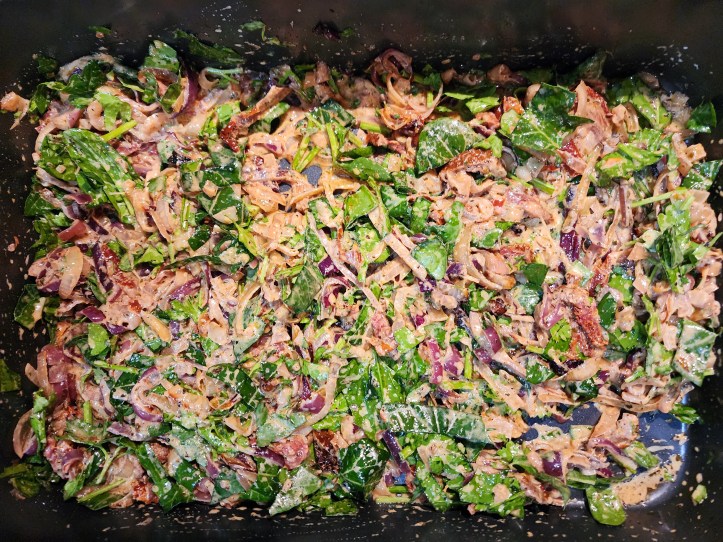 Top down view of a roasting tray full of chopped red onions, spinach, and sundried tomatoes.