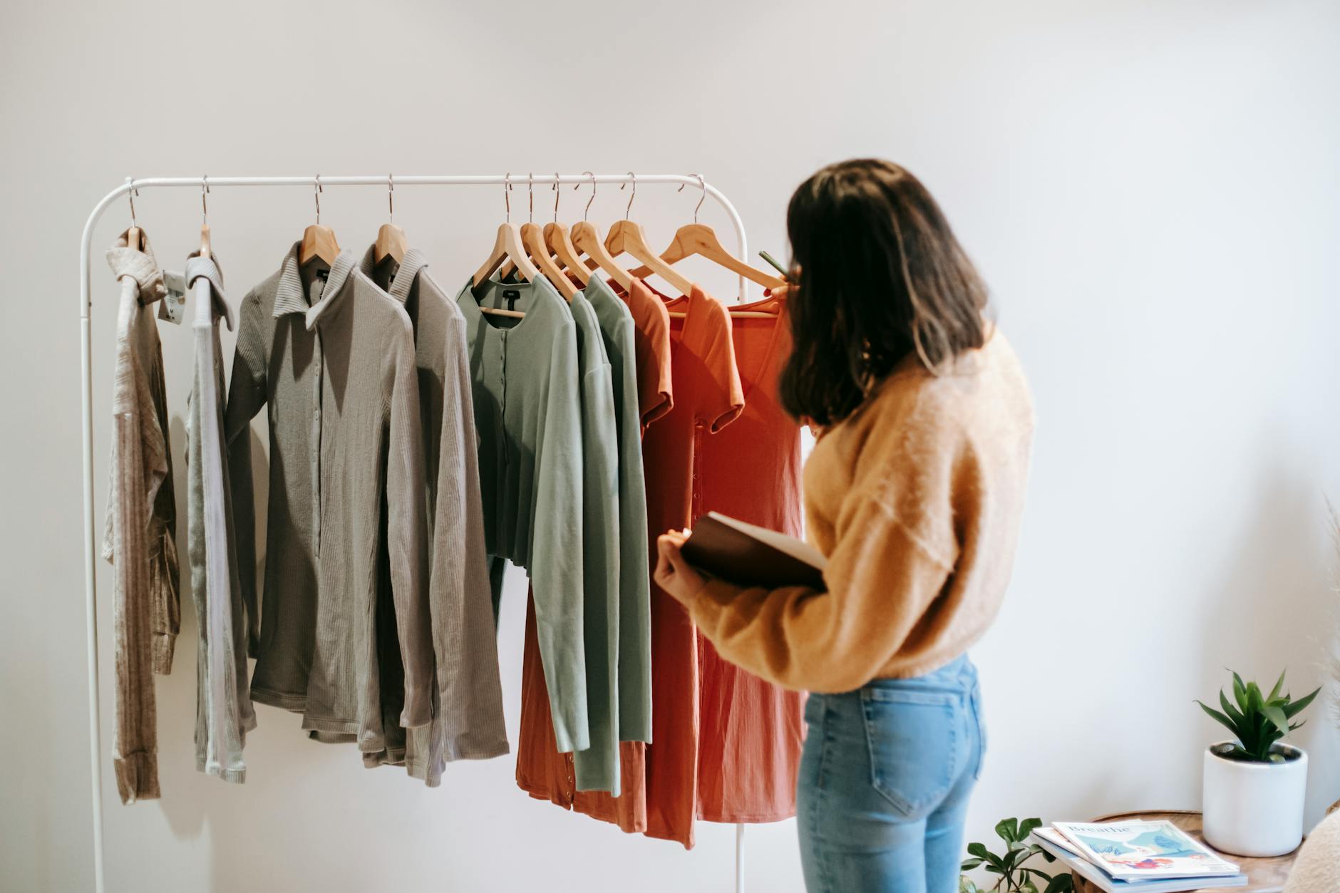 A woman with short brown hair examines clothes on a rail, against a white background.