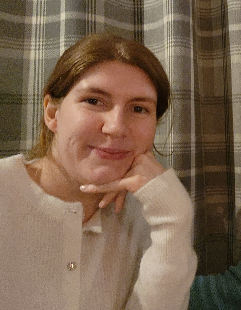 Helen wearing a cream coloured cardigan with her hair tied back, resting her head on one hand.