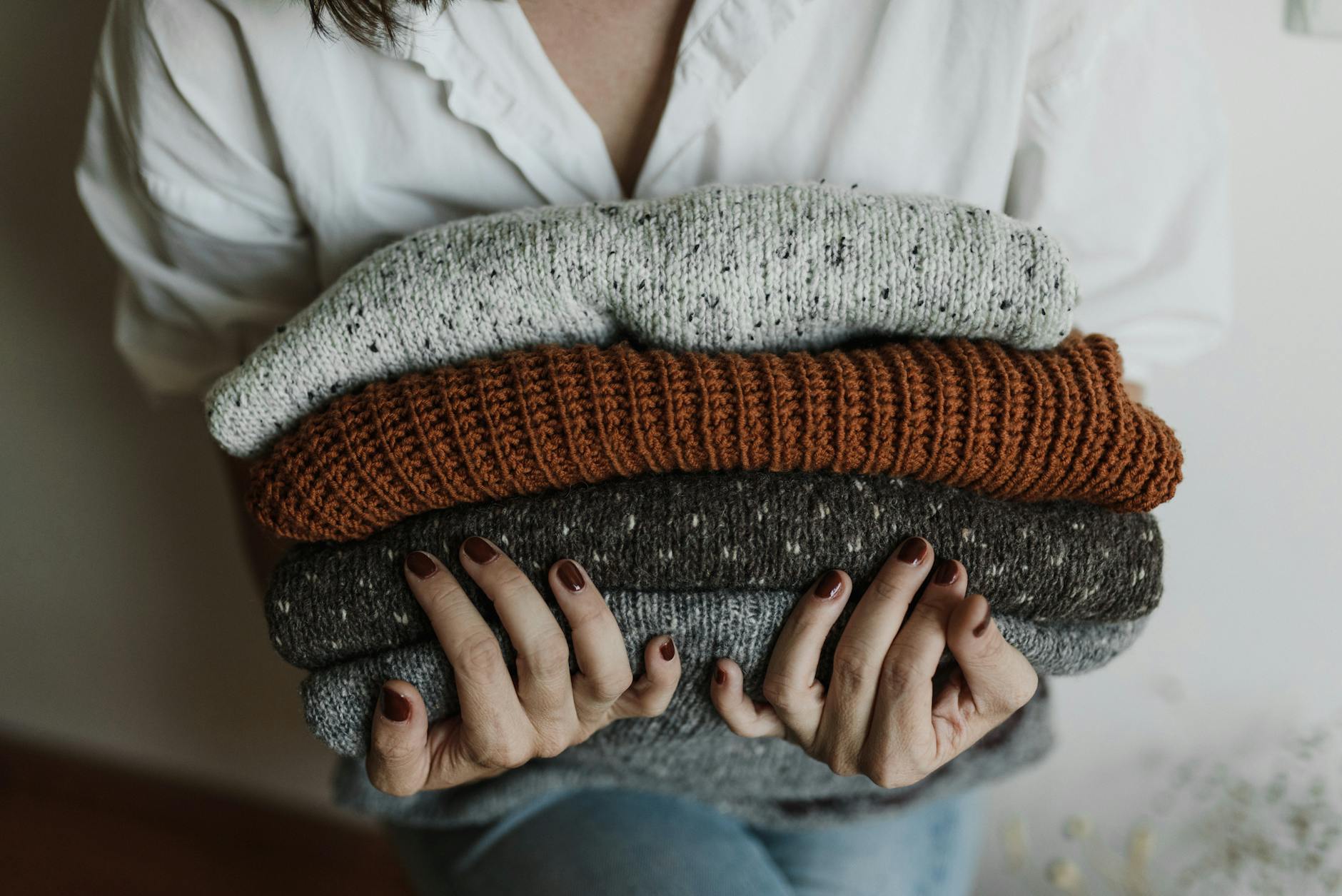 Woman holding a pile of similar knit jumpers.